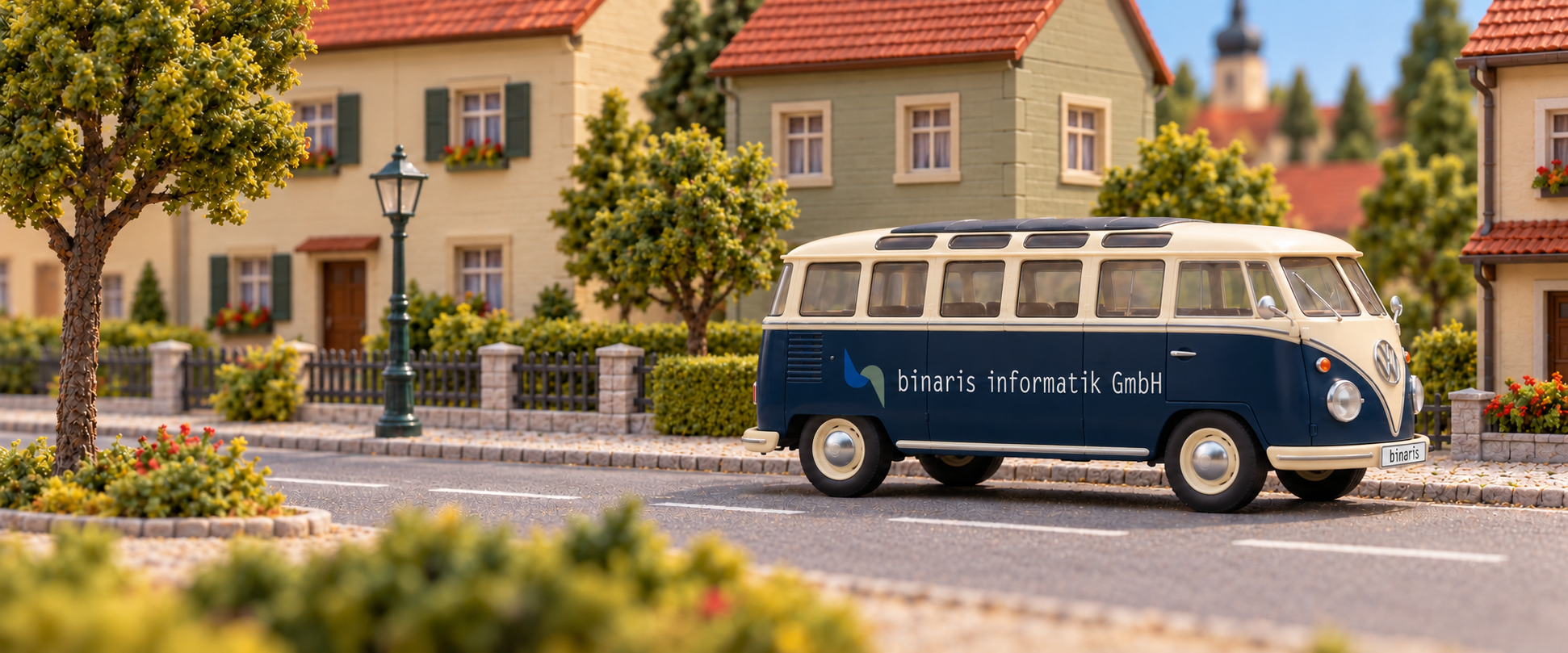 Ein dunkelblau-cremefarbener VW T1 Samba mit binaris-Beschriftung als Kunststoffmodell in einer detailreichen Modellbausiedlung. KI-generierte Abbildung.